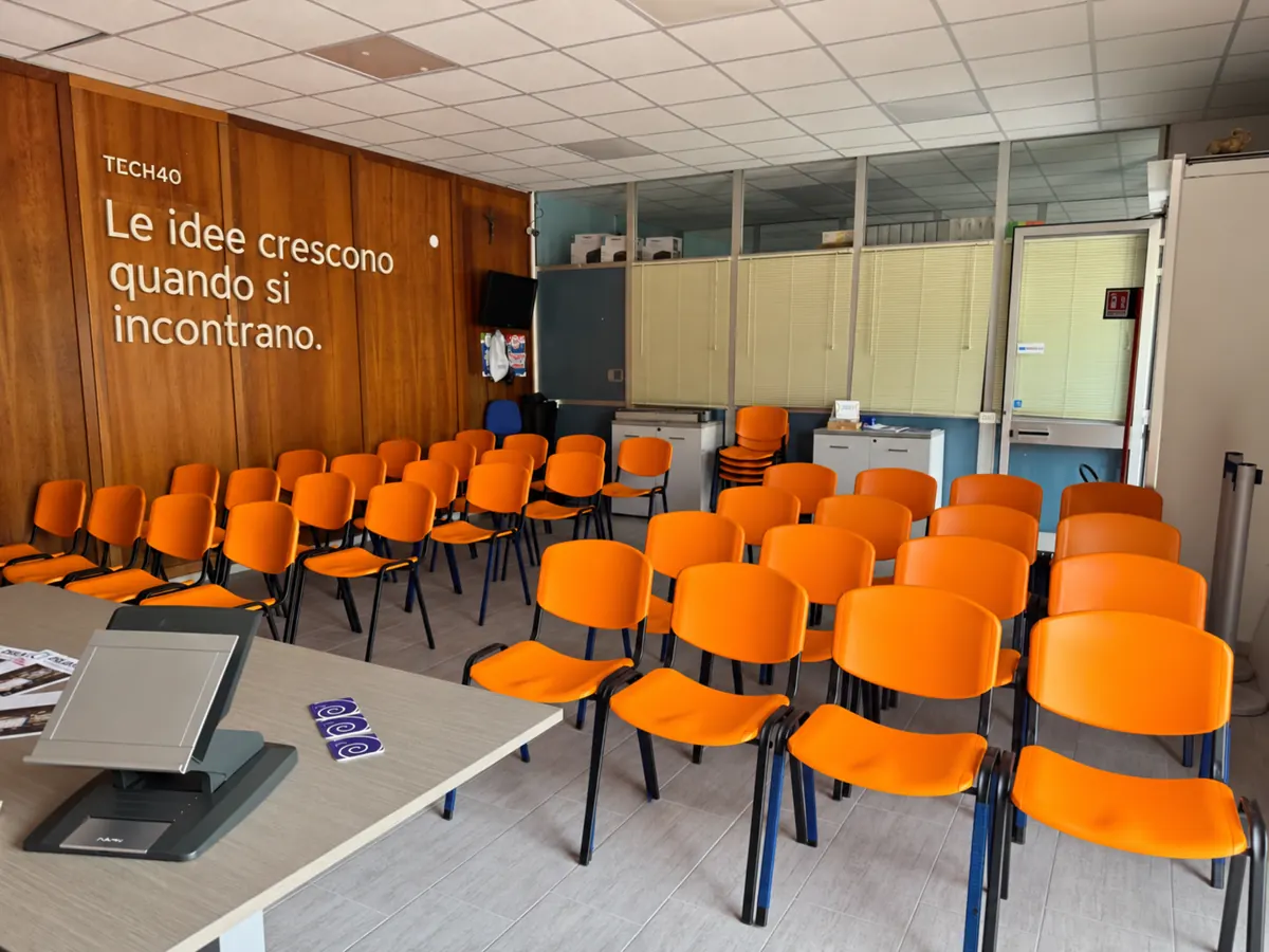 Sala TECH40 con sedute arancioni e lo slogan sul muro: Le idee crescono quando si incontrano.